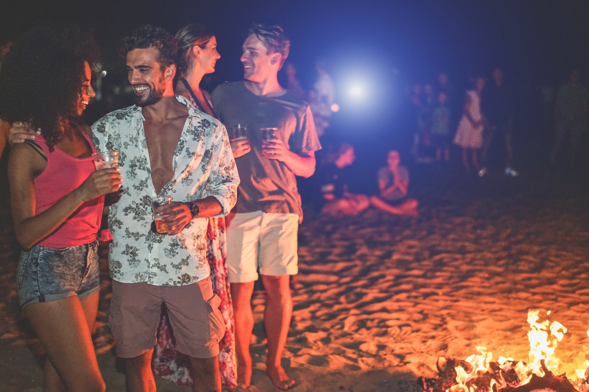 Friends sharing drinks around a beach bonfire at night